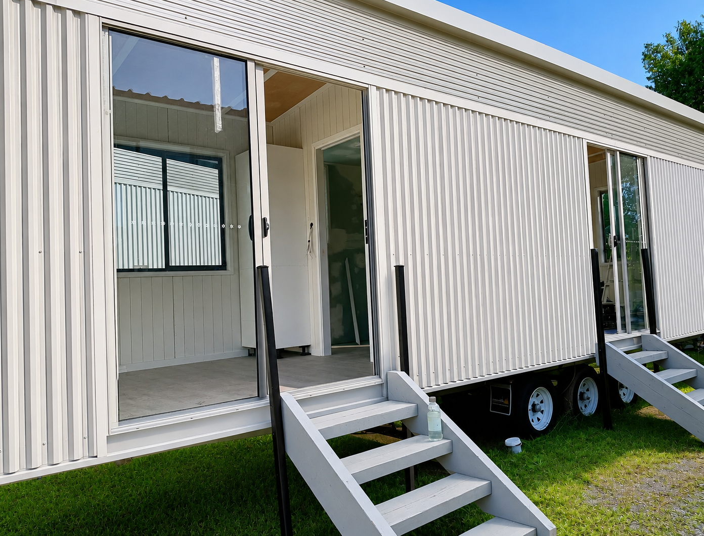 White tiny home with open sliding doors and entry steps on a sunny day