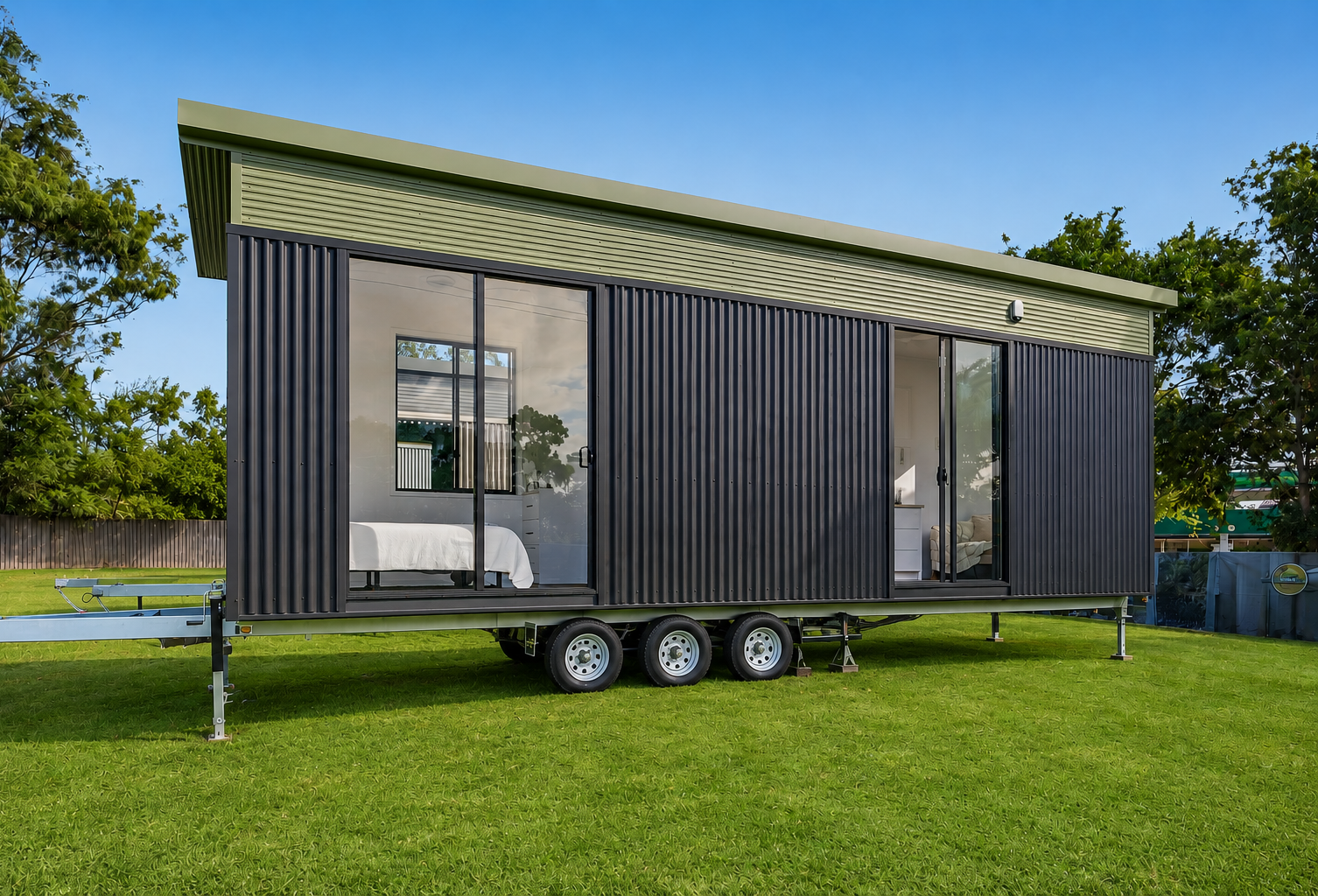Black and olive-green tiny home on a triple-axle trailer on green lawn