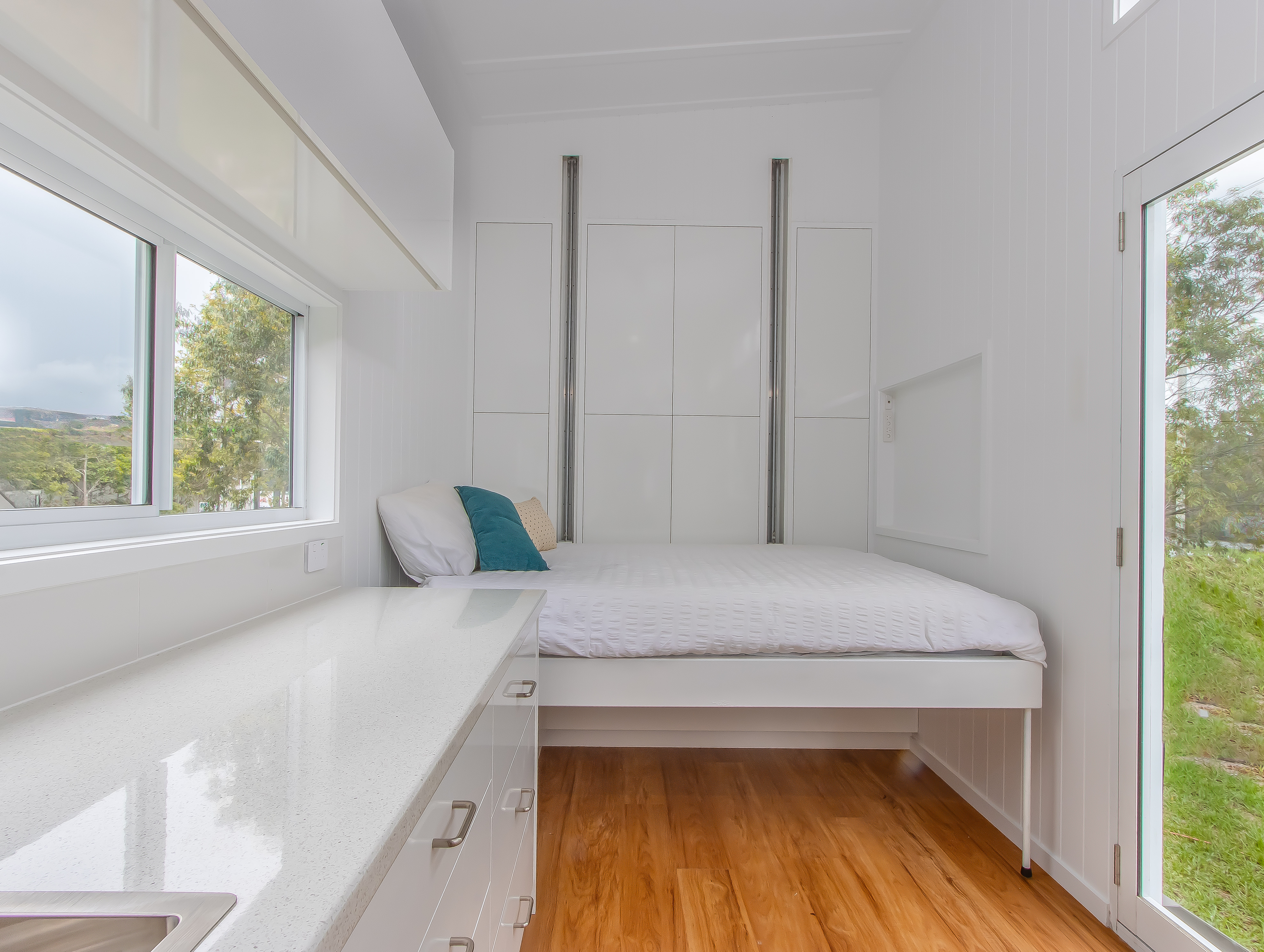 Bright white tiny home bedroom with built-in bed and storage